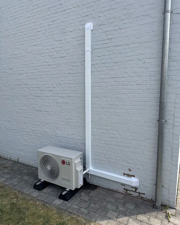 LG airco buitenunit op voetblok tegen een witte gevel, met nette leidingkoker