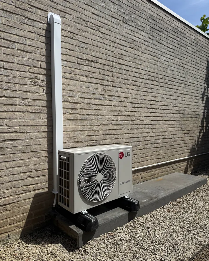 LG airco buitenunit op voetblok tegen een sierbaksteenmuur
