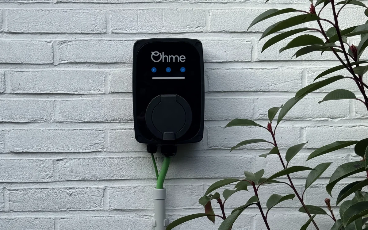 Ohme laadpunt aan een wit geschilderde gevel, met de kabelkoker netjes naar beneden weggewerkt